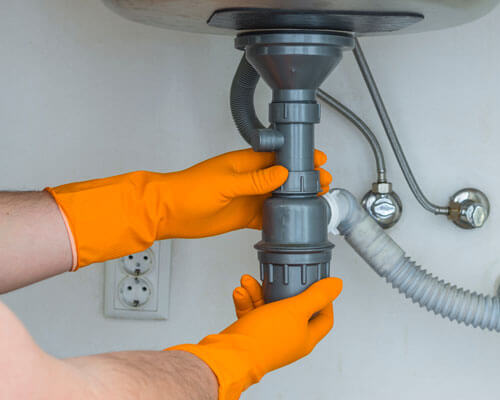 Plumber In Orange Rubber Gloves Clearing A Clogged Drain Under T