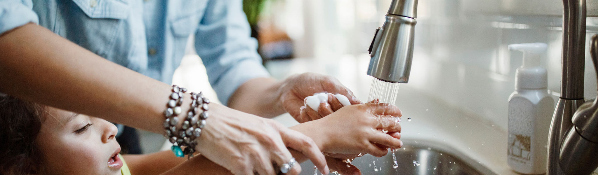 Midsection Of Mother With Daughter Washing Hands In Kitchen Sink At Home