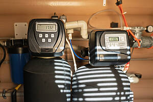 Modern Water Filtration And Heating System Installed In A Utility Room, Featuring Digital Control Panels And Various Tanks And Pipes Under Warm Indoor Lighting.