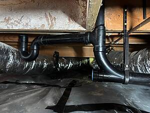 Basement utility area showing black PVC drainage pipes with a U-shaped trap and foil-insulated ducts above.