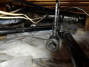 Open attic space with exposed HVAC ducts, flexible foil ducting, black plastic pipes, and hanging metal supports among wooden joists.