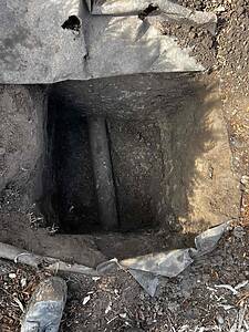 Deep dirt trench with a cylindrical pipe at the bottom and gray stone slabs along the edge.