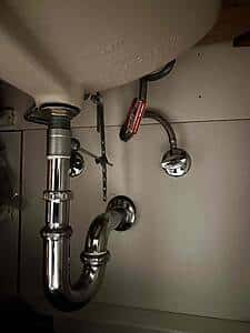 Under-sink plumbing with a chrome P-trap and supply lines visible under a kitchen sink.