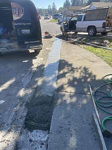 Trench dug along a residential street with building materials, hoses, and two pickup trucks nearby.