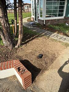 Brick front steps with sunglasses resting on the ledge; shovel propped against a tree in a dirt yard near a house with bay windows.