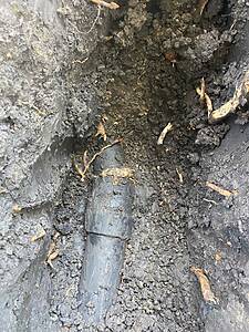 Underground scene with a dark pipe running through loose soil and exposed roots after digging.