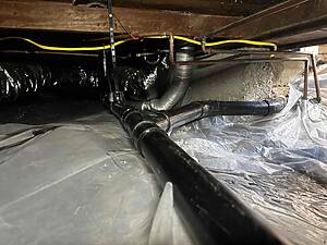 Basement crawl space showing exposed copper pipes, black ductwork, and yellow electrical cables running along a wooden beam.