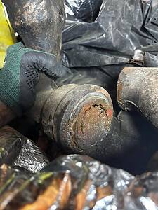 Gloved hand gripping a rusted metal bolt among debris and plastic sheeting in a junk pile