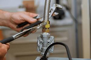 Close-up of a technician tightening a brass valve fitting on a gas line with a wrench and pliers nearby for leverage.