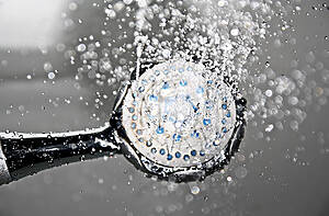Close-up of a shower head spraying water droplets in midair, chrome finish.