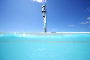 Chrome pool fountain jet rising from a turquoise pool against a clear blue sky