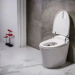 White modern toilet with open lid in a marble-tiled bathroom; a red decorative sculpture stands to the left on a black base.