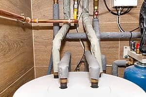 Close-up of copper water pipes with valves and insulated lines in a utility room.